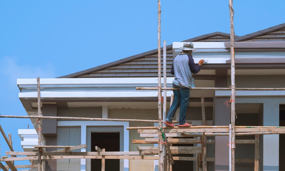 Asian builder worker on wooden scaffolding is painting roof structure of modern house